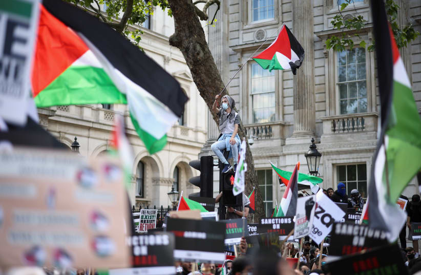  A protester holds a flag as he sits on a traffic light post during a pro-Palestine demonstration outside Downing Street in London, Britain, June 12, 2021 (photo credit: REUTERS/HENRY NICHOLLS)