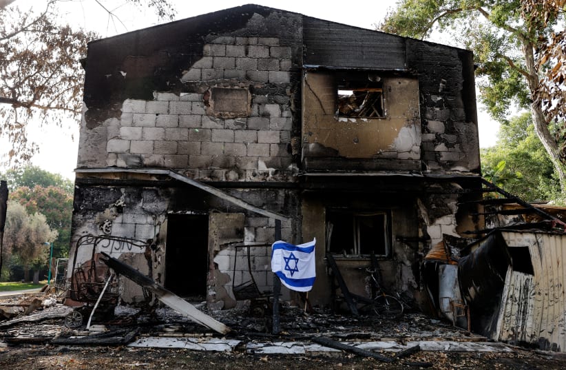 An Israeli flag flutters in front of the remains of a building, following a deadly infiltration by Hamas gunmen from the Gaza Strip, in Kibbutz Beeri in southern Israel October 22, 2023 (photo credit: AMIR COHEN/REUTERS)