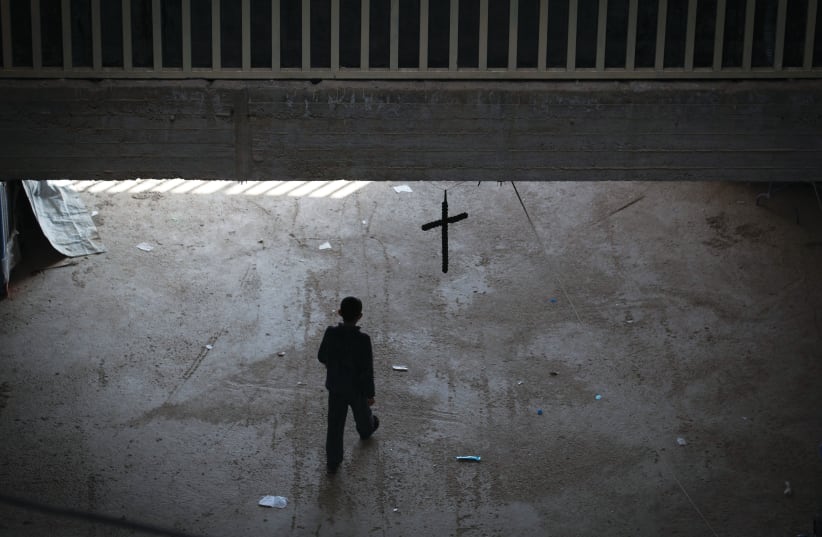  AN IRAQI Christian who fled from his home due to ISIS’s advance walks beneath a cross erected inside an unfinished shopping mall – which had become home to hundreds of displaced people, in Erbil, Iraq, 2014 (photo credit: Matt Cardy/Getty Images)