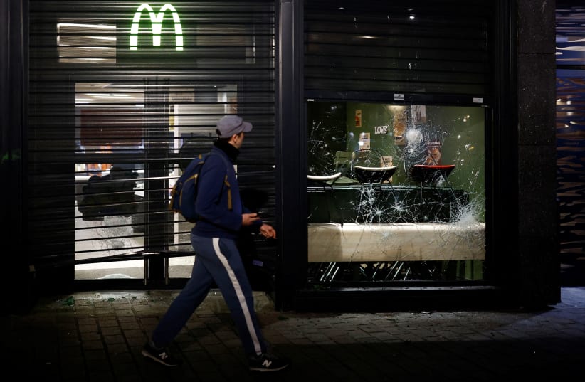 A man walks by while looking at a vandalized McDonald's as demonstrators gather in Nantes to protest after French Prime Minister Elisabeth Borne used the article 49.3, a special clause in the French Constitution, to push the pensions reform bill through the National Assembly without a vote by lawmak (photo credit: REUTERS/STEPHANE MAHE)