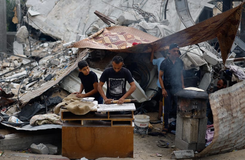 Palestinians prepare food next to destroyed buildings in Khan Younis, in the southern Gaza Strip, on November 13, 2023 (photo credit: REUTERS/MOHAMMED SALEM)