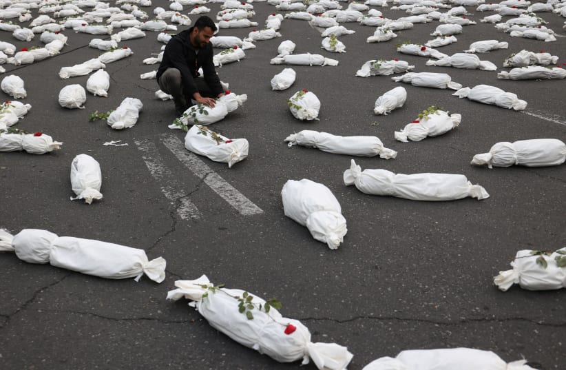 An Iranian man sits next to the symbolic shrouds of Gaza children's dead bodies during a gesture in a street in Tehran, Iran November 13, 2023. (photo credit: MAJID ASGARIPOUR/WANA/REUTERS)