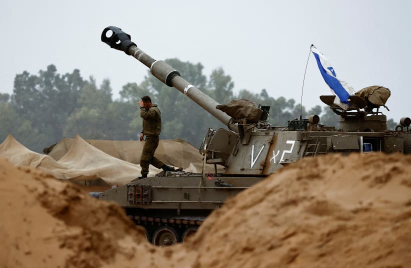 An Israeli soldier walks near a mobile artillery unit near the northern Gaza border, in southern Israel, November 19, 2023 (photo credit: REUTERS/AMIR COHEN)