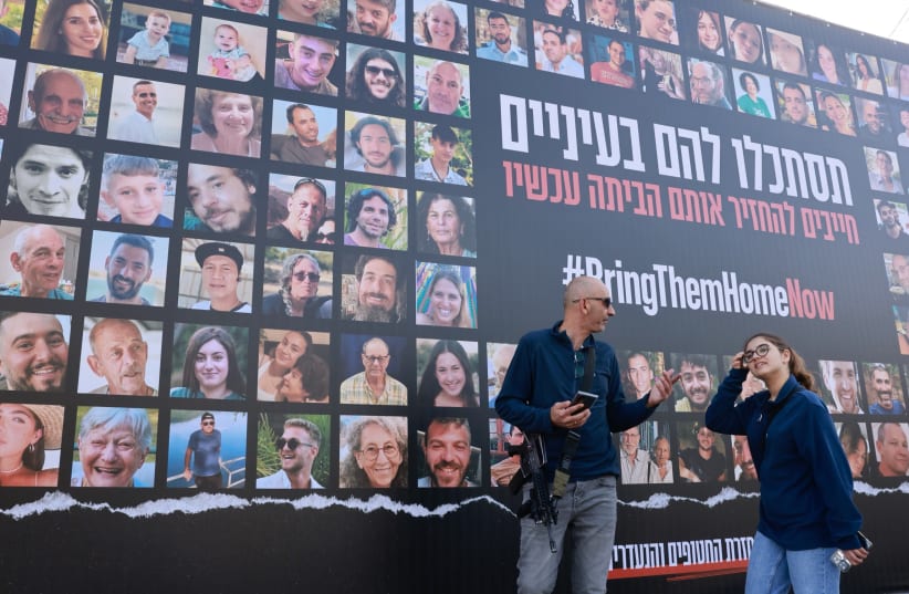 People walk next to pictures of civilians held hostage by Hamas terrorists in Gaza, in Jerusalem, November 22, 2023 (photo credit: MARC ISRAEL SELLEM/THE JERUSALEM POST)