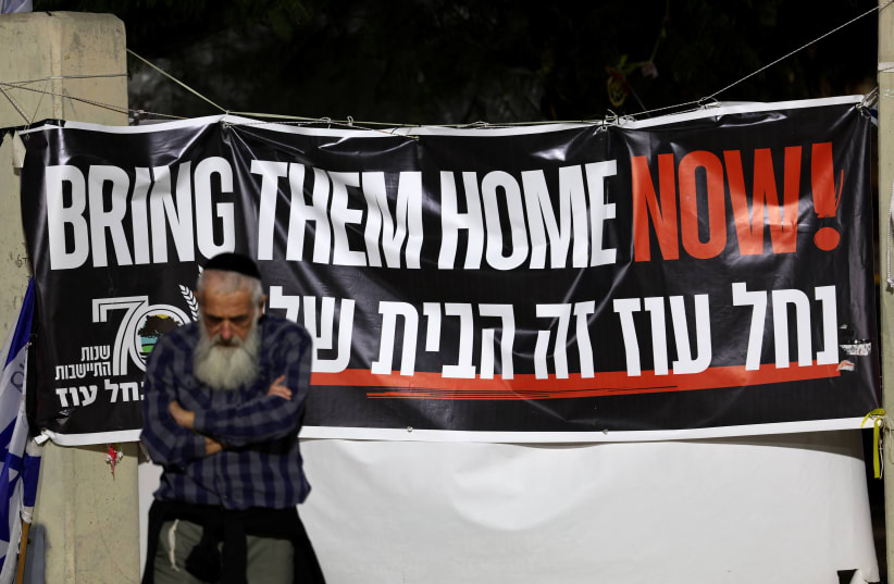  A man stands next to a banner as hostages are expected to be released by the Palestinian militant group Hamas, amid a hostages-prisoners swap deal between Hamas and Israel, in Tel Aviv, Israel, November 26, 2023 (photo credit: REUTERS/ATHIT PERAWONGMETHA)