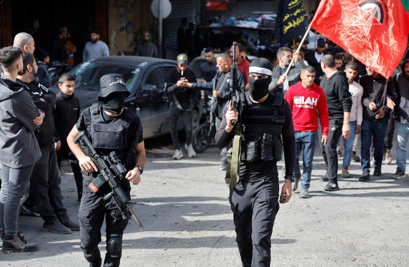 Armed men walk as the bodies of Palestinians (not pictured), who were killed during an Israeli raid, are carried through the streets in Jenin, in the West Bank. November 26, 2023. (photo credit: RANEEN SAWAFTA/REUTERS)