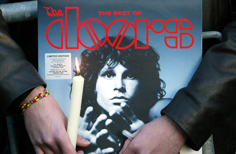  A fan holds an album by the seventies rock group The Doors and a candle near the tomb of late singer Jim Morrison during a ceremony marking what would have been Morrison's 60th birthday at the Pere Lachaise cemetery in Paris, December 8, 2003. (photo credit: REUTERS)