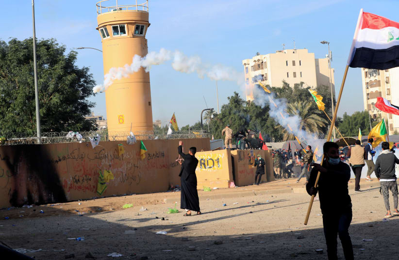 Protesters and militia fighters throw back a tear gas canister used by U.S. Embassy security men during a protest to condemn air strikes on bases belonging to Hashd al-Shaabi (paramilitary forces), outside the embassy in Baghdad, Iraq January 1, 2020. (photo credit: THAIER AL-SUDANI/REUTERS)