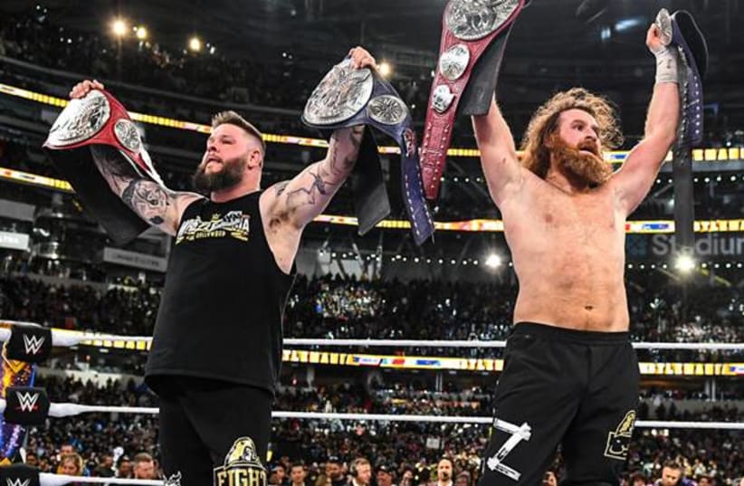  WWE superstar Sami Zayn (right) is seen alongside longtime partner and rival Kevin Owens holding professional wrestling titles aloft in a ring. (photo credit: Wikimedia Commons)