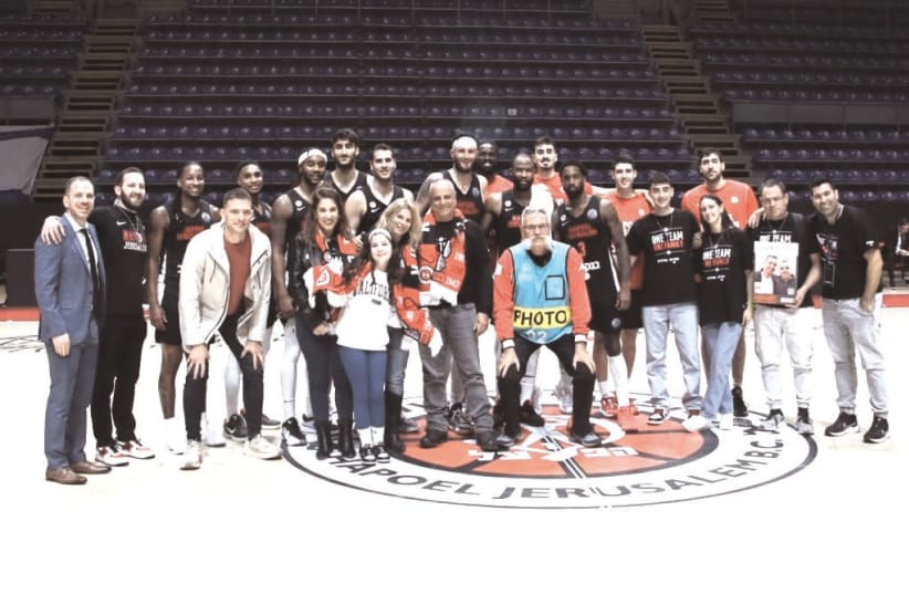  HAPOEL JERUSALEM players and management pose on the Pionir Arena court in Belgrade with a group of fans – including released hostage Ofir Engel and his family – who were flown in for the Reds’ 71-61 Champions League win over PAOK.  (photo credit: COURTESY HAPOEL JERUSALEM)