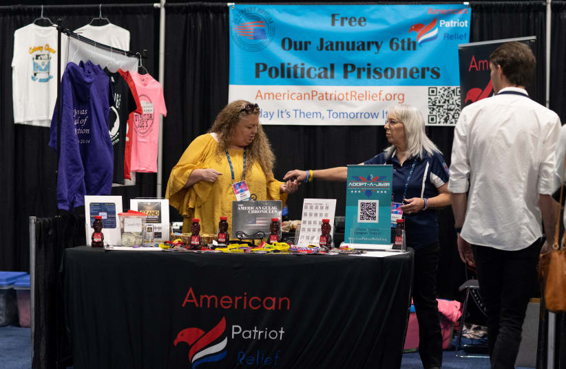  People stand at the table for American Patriot Relief, in front of a sign that reads Free Our January 6th Political Prisoners, as conservative leaders and personalities attend Turning Point USA's AmericaFest 2023 in Phoenix, Arizona, US December 16, 2023.  (photo credit: REUTERS/Caitlin O’Hara)