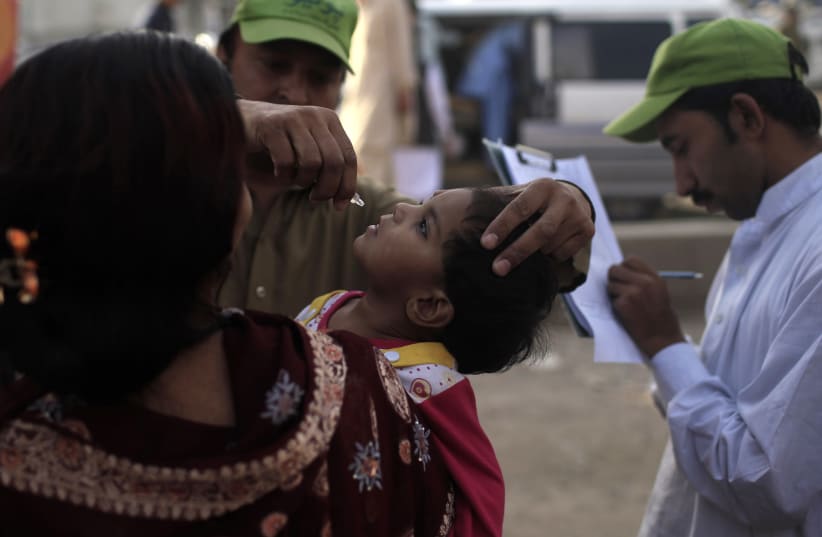  A polio worker administers polio vaccine to a child, who arrived from the Khyber-Pakhtunkhwa province, during a vaccination campaign at a bus stop in Rawalpindi May 13, 2014. (photo credit: REUTERS/Sara Farid)