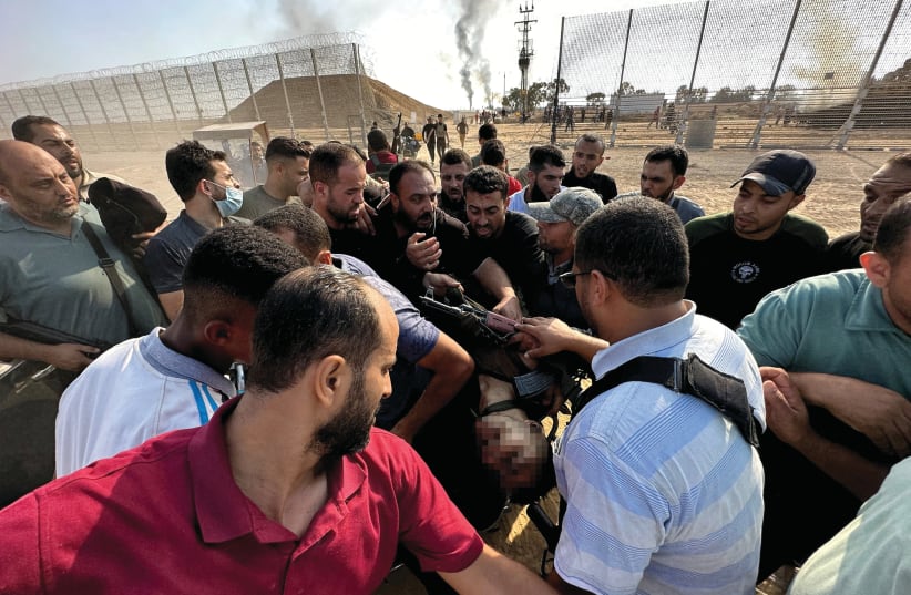  A REUTERS photo taken by Abu Mostafa on Oct. 7: Palestinians carry the body of an Israeli soldier slaughtered by Hamas after being pulled from a tank. (photo credit: Mohammed Fayq Abu Mostafa/Reuters)