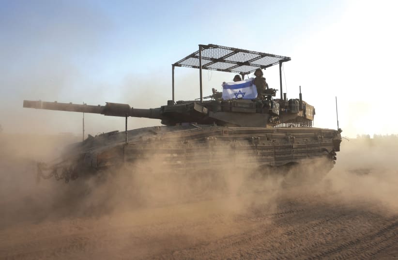  IDF SOLDIERS hold an Israeli flag as they patrol in a tank near the border with Gaza this week (photo credit: RONEN ZVULUN/REUTERS)