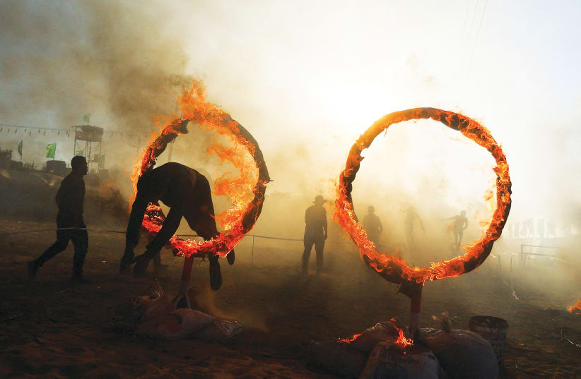  A YOUNG Palestinian jumps through a ring of fire during a military exercise at a summer camp organized by Hamas, in Khan Yunis in August. (photo credit: IBRAHEEM ABU MUSTAFA/REUTERS)