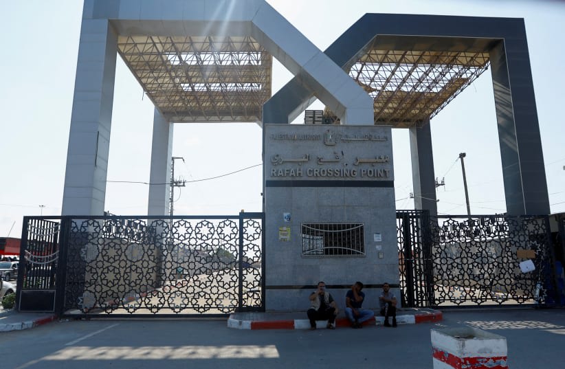 Varios palestinos con doble nacionalidad esperan sentados frente a las puertas del paso fronterizo de Rafah con Egipto con la esperanza de obtener permiso para salir de Gaza, en medio del actual conflicto palestino-israelí, en Rafah, en el sur de la Franja de Gaza. 14 de octubre de 2023. (photo credit: IBRAHEEM ABU MUSTAFA/REUTERS)
