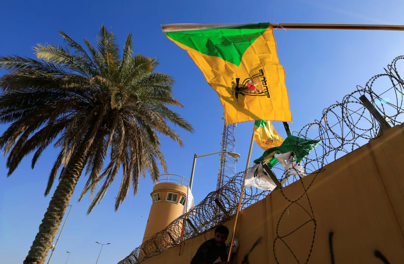  Un miembro de Hashd al-Shaabi (fuerzas paramilitares) sostiene una bandera del grupo miliciano Kataib Hezbollah durante una protesta para condenar los ataques aéreos en sus bases, fuera de la puerta principal de la Embajada de Estados Unidos en Bagdad, Irak, el 31 de diciembre de 2019. (photo credit: REUTERS/THAIER AL-SUDANI)
