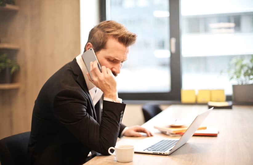  Un hombre habla por teléfono sentado en la mesa de su despacho. (Ilustrativo) (photo credit: PXFUEL)