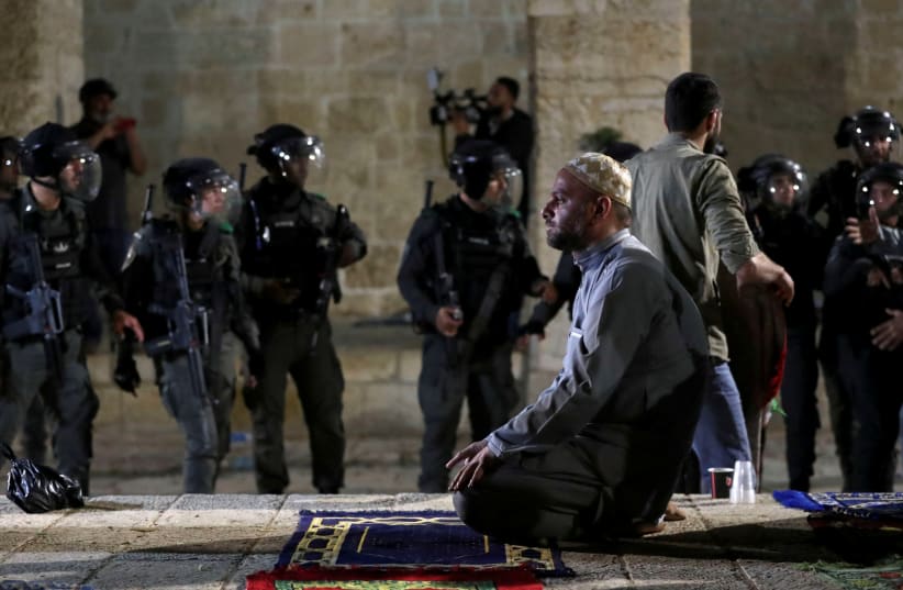  Un palestino reza mientras la policía israelí se reúne durante los enfrentamientos en el recinto que alberga la mezquita de Al-Aqsa, conocido por los musulmanes como Noble Santuario y por los judíos como Monte del Templo. 7 de mayo de 2021. (photo credit: AMMAR AWAD/REUTERS)