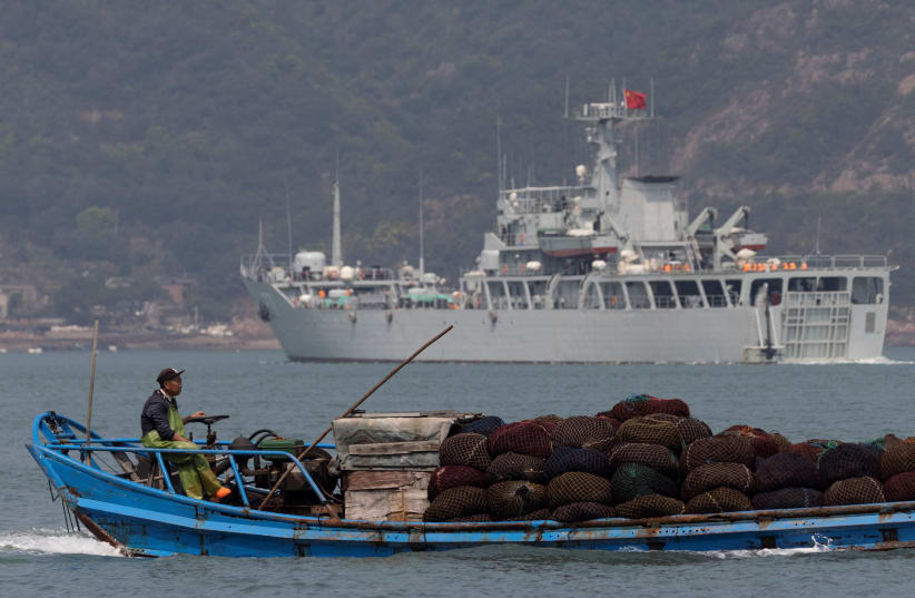 A fishing boat sails past a Chinese warship during a military drill off the Chinese coast near Fuzhou, Fujian Province, across from the Taiwan-controlled Matsu Islands, China, April 11, 2023. (photo credit: THOMAS PETER/REUTERS)