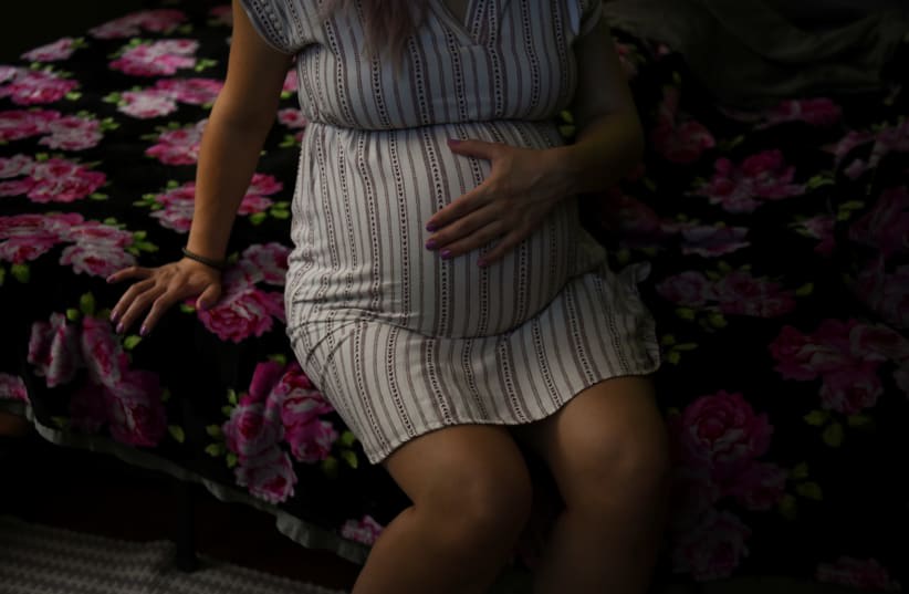  Una mujer embarazada se sienta en una cama sujetándose el vientre. (photo credit: CALLAGHAN O'HARE/REUTERS)