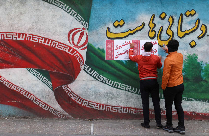  Hombres iraníes colocan carteles de campaña en una pared durante el último día de campaña electoral en Teherán, Irán, 28 de febrero de 2024. (photo credit: MAJID ASGARIPOUR/WANA (WEST ASIA NEWS AGENCY) VIA REUTERS)