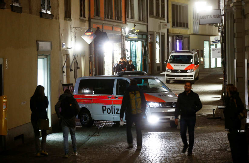  People walk past as Swiss police vehicles stand by to prevent expected illegal gatherings amid restrictions due to the coronavirus (COVID-19) pandemic, in the old town of Zurich, Switzerland, April 9, 2021. (photo credit: Arnd Wiegmann/Reuters)