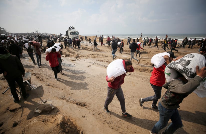   Palestinians carry bags of flour they grabbed from an aid truck near an Israeli checkpoint, as Gaza residents face crisis levels of hunger, amid the ongoing conflict between Israel and Hamas, in Gaza City, February 19, 2024.  (photo credit: REUTERS/Kosay Al Nemer/File Photo)