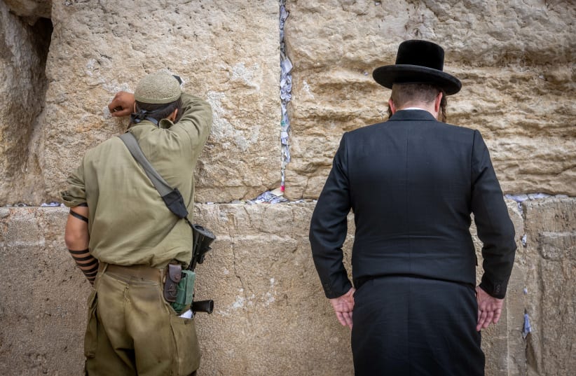  An Israeli soldier prays next to an ultra orthodox Jewish man at the Western Wall, in Jerusalem (photo credit: Chaim Goldberg/Flash90)