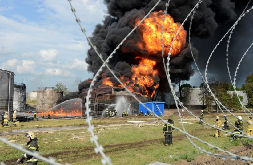  Una vista a través de alambres de púas muestra el humo del fuego que se eleva por encima de un tanque de combustible en llamas de un depósito de petróleo en Voronezh, Rusia, 24 de junio de 2023. (photo credit: STRINGER/ REUTERS)
