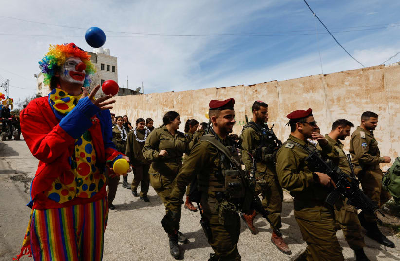  Un colono israelí participa en las celebraciones de la festividad judía de Purim, mientras soldados de las FDI patrullan, en Hebrón, Cisjordania, el 7 de marzo de 2023. (photo credit: MUSSA QAWASMA/REUTERS)