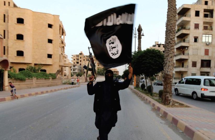  Un MIEMBRO del ISIS ondea la bandera del grupo en Raqqa (photo credit: REUTERS)