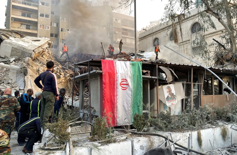  Una bandera iraní cuelga mientras el humo se eleva después de lo que los medios de comunicación iraníes dijeron que era un ataque israelí contra un edificio cerca de la embajada iraní en Damasco, Siria 1 de abril 2024. (photo credit: FIRAS MAKDESI/REUTERS)