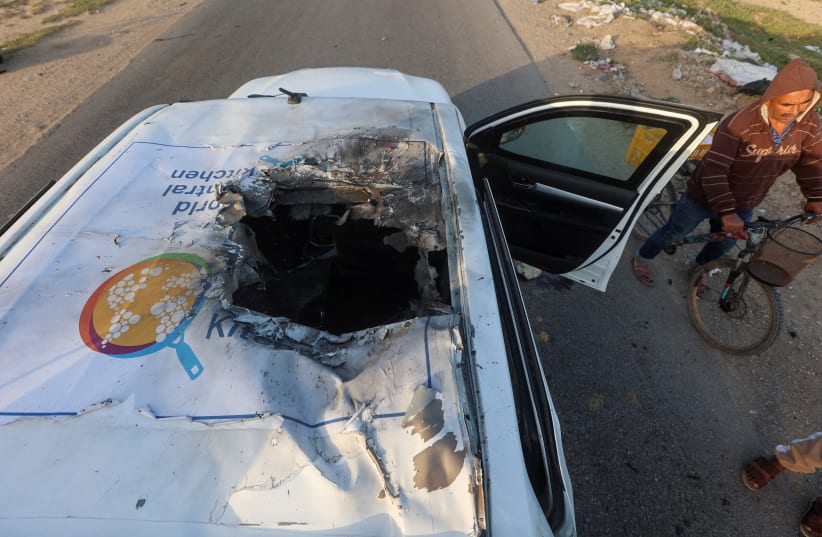  A Palestinian man rides a bicycle past a damaged vehicle where employees from the World Central Kitchen (WCK) were killed in an Israeli airstrike, in the central Gaza Strip April 2, 2024.  (photo credit: Ahmed Zakot/Reuters)