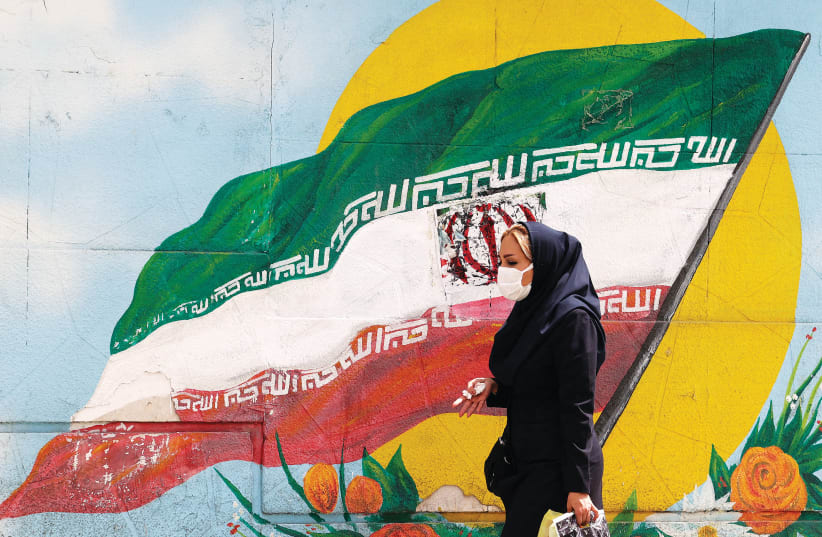  UNA MUJER pasa junto a una bandera iraní pintada en una pared de una calle de Teherán a principios de esta semana. (photo credit: Atta Kenare/AFP via Getty Images)