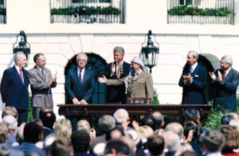 El presidente de la OLP, Yasser Arafat (tercero a la derecha), gesticula hacia el primer ministro Yitzhak Rabin (tercero a la izquierda) mientras el presidente estadounidense Bill Clinton (en el centro) se interpone entre ambos, tras la firma de los Acuerdos de Oslo el 13 de septiembre de 1993. (photo credit: GARY HERSHORN/REUTERS)