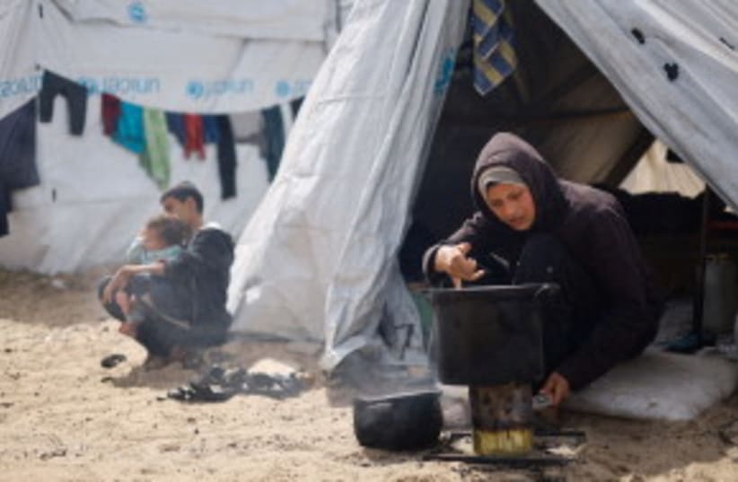 Una mujer cocina mientras palestinos desplazados por ataques israelíes se refugian en Rafah, en medio del conflicto entre Israel y Hamás en Gaza, el 6 de marzo de 2024. (photo credit: REUTERS/MOHAMMED SALEM)