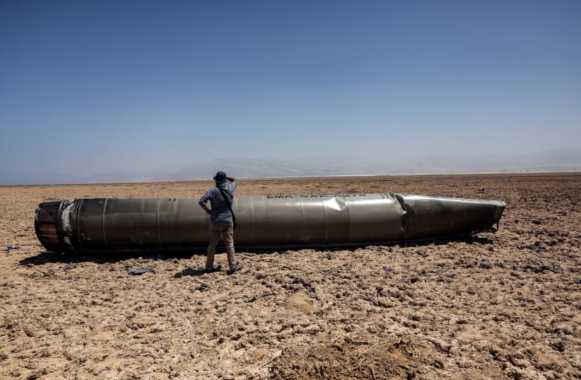  A man stands next to the apparent remains of a ballistic missile, as it lies in the desert near the Dead Sea, following a massive missile and drone attack by Iran on Israel, in southern Israel April 21, 2024  (photo credit: REUTERS/Ronen Zvulun)