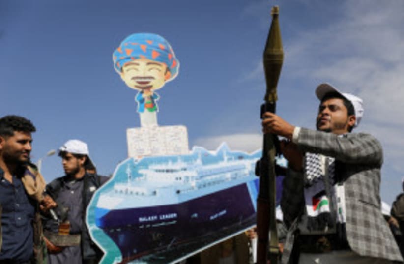 Seguidor houthi sostiene lanzacohetes, mientras otros llevan pancarta del carguero Galaxy Leader capturado por los houthis, en desfile de "ejército popular" en Saná, Yemen, 7 de febrero de 2024. (photo credit: REUTERS/KHALED ABDULLAH)