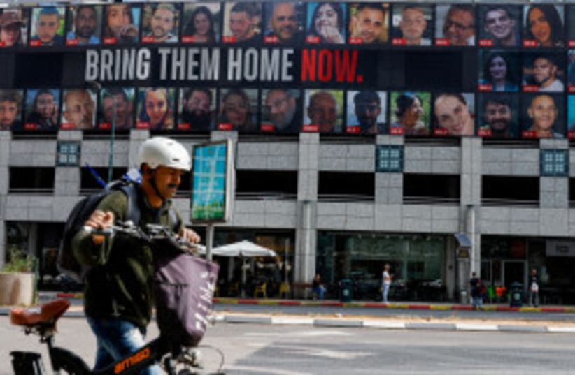 Un hombre empuja una bicicleta cerca de una valla publicitaria con imágenes de los rehenes secuestrados en el mortífero ataque del 7 de octubre contra Israel por el grupo islamista palestino Hamás desde Gaza, en Tel Aviv, Israel 18 de marzo 2024. (photo credit: CARLOS GARCIA RAWLINS/REUTERS)