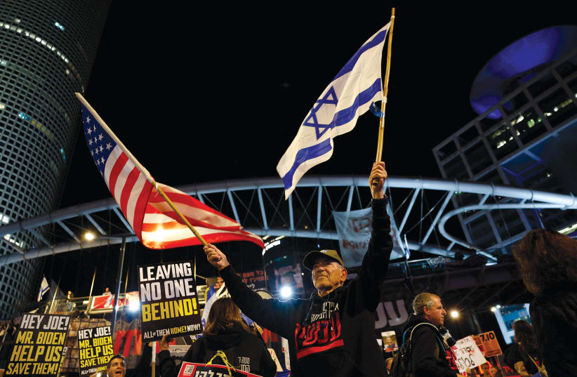  Un manifestante sostiene banderas estadounidenses e israelíes durante una protesta para pedir la liberación de los rehenes, Tel Aviv, 9 de marzo. (photo credit: REUTERS/CARLOS GARCIA RAWLINS)