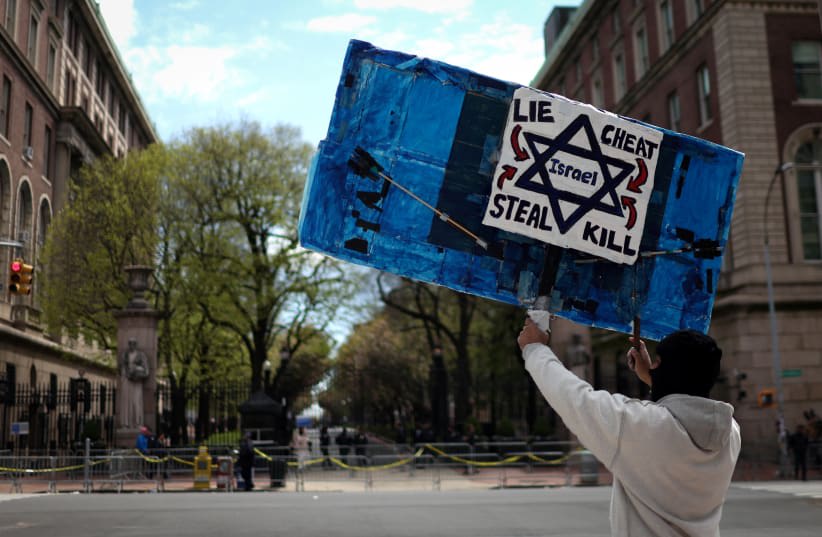  Un manifestante sostiene una pancarta frente al campus de la Universidad de Columbia con un campamento de protesta estudiantil en apoyo a los palestinos, durante el actual conflicto entre Israel y el grupo islamista palestino Hamás, en la ciudad de Nueva York, Estados Unidos, 25 de abril de 2024. (photo credit: Mike Segar/Reuters)