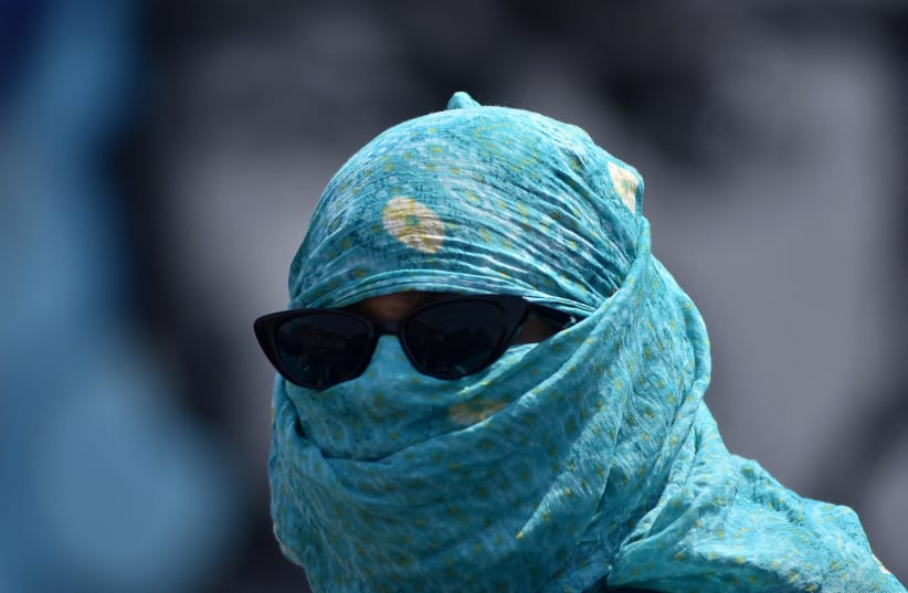 A woman has her face covered with a scarf to protect her from the heat on a road during a hot summer day in Bhubaneswar, India, May 3, 2024.  (photo credit: STRINGER/ REUTERS)