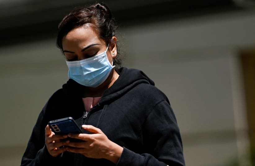  Una señora con mascarilla mira su teléfono en medio de la ola Omicron de la enfermedad por coronavirus (COVID-19) en Singapur, el 17 de febrero de 2022. (photo credit: REUTERS/CAROLINE CHIA)