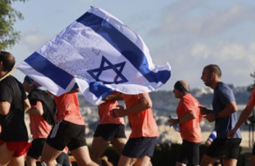  Participantes en el Maratón de Jerusalén avanzan por el recorrido de la carrera, ondeando una bandera de Israel firmada, 8 de marzo de 2024. (photo credit: MARC ISRAEL SELLEM/THE JERUSALEM POST)
