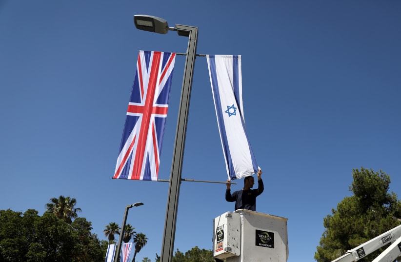   Un trabajador del municipio de Jerusalén cuelga una bandera israelí junto a la bandera británica, la Union Jack, mientras se encuentra en una plataforma cerca de la residencia presidencial de Israel en Jerusalén antes de la próxima visita del príncipe Guillermo de Gran Bretaña, 25 de junio de 2018 (photo credit: AMMAR AWAD/REUTERS)