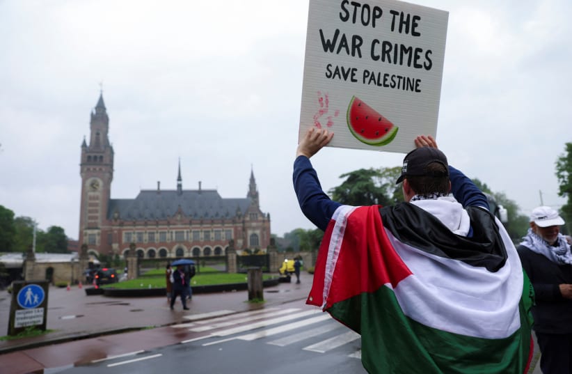 A protester draped in a Palestinian flag holds up a sign at a protest in support of Palestinians in Gaza outside the International Court of Justice (ICJ), on the day of a ruling on South Africa's request to order a halt to Israel's Rafah offensive in Gaza as part of a larger case brought before the  (photo credit: JOHANNA GERON/REUTERS)
