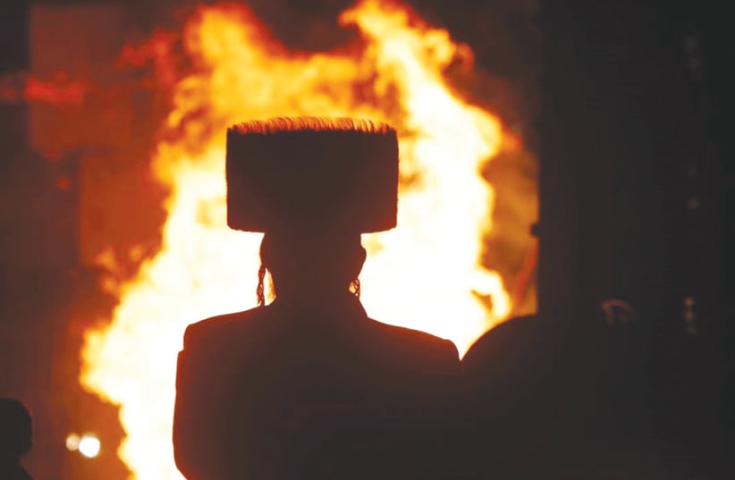  A MAN looks at a Lag Ba’omer bonfire on Saturday night in Jerusalem. The joy and warmth of Lag Ba’Omer stand in stark contrast to the pain and sorrow of the past months, the writer notes.  (photo credit: MARC ISRAEL SELLEM/THE JERUSALEM POST)