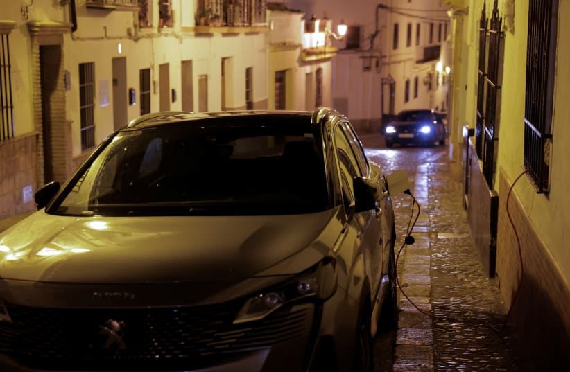  Un vehículo eléctrico híbrido enchufable Peugeot 3008 de la empresa de alquiler de coches OK Mobility, está aparcado en una calle, mientras se carga con un cable conectado a un enchufe doméstico dentro de un apartamento turístico, en Ronda, España, el 2 de mayo de 2024. (photo credit: REUTERS/JON NAZCA)