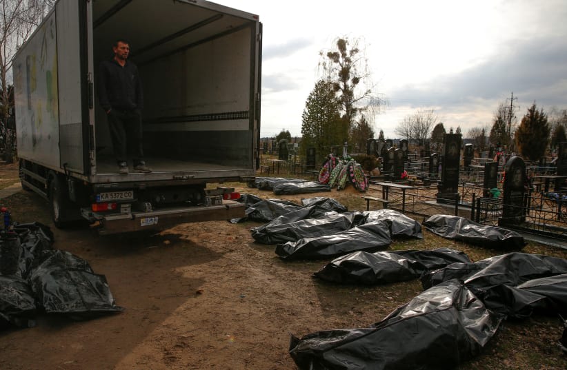  Un empleado de un servicio funerario observa los cadáveres de civiles, recogidos en las calles para llevarlos al cementerio local, mientras continúa el ataque de Rusia contra Ucrania, en la ciudad de Bucha, a las afueras de Kiev, Ucrania, el 6 de abril de 2022. (photo credit: Oleg Pereverzev/Reuters)
